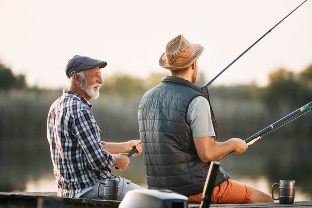 Happy senior man enjoying in freshwater fishing with his son in nature.